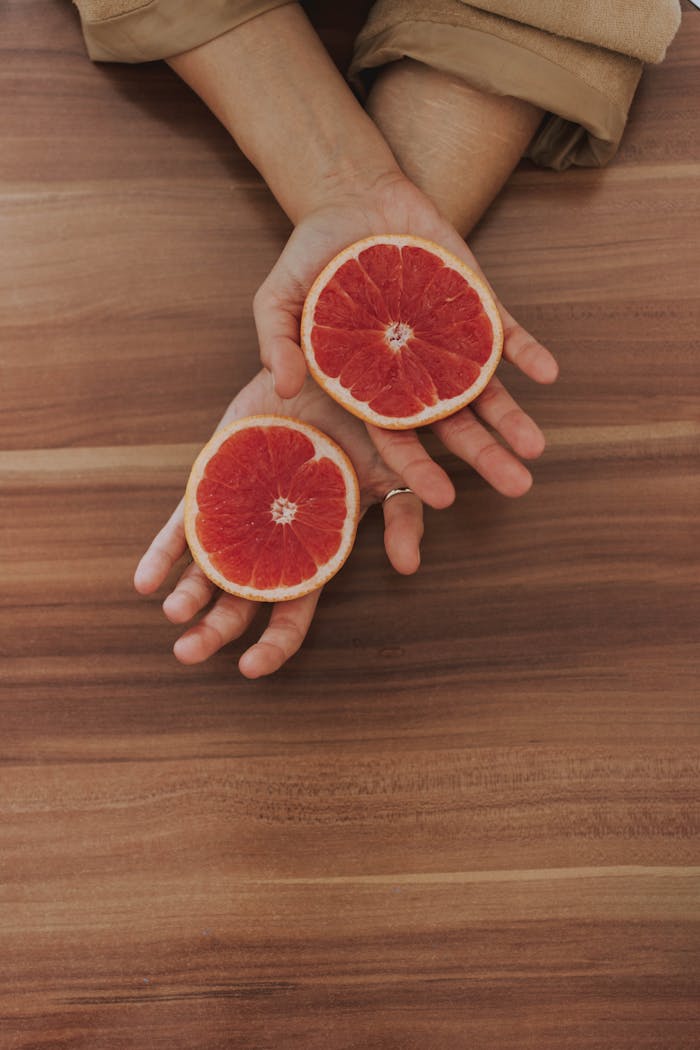 Two fresh grapefruit halves resting in hands over a wooden table, showcasing vibrant and juicy fruit.